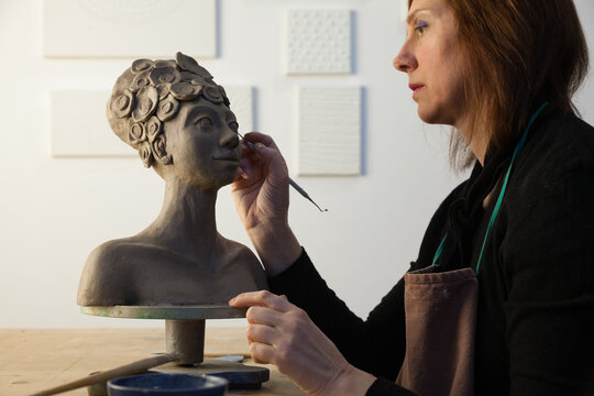 side view of an artist working on details of a clay statue