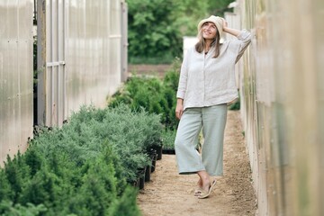 A beautiful happy young girl stand in greenhouse. Woman in natural linen clothes and a hat in the...