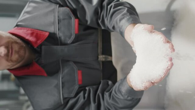 Vertical midsection footage of plant worker pouring handful of transparent polypropylene granules
