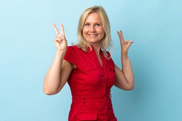 Middle age woman isolated on blue background showing victory sign with both hands