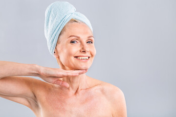 Portrait of smiling senior woman feeling soft skin with hand after spa bath. Mature woman draped in...
