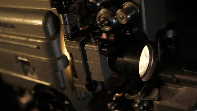 The retro movie projector turns on. The mechanism scrolls the film by a glowing lamp in the lens. The projector is turned off.