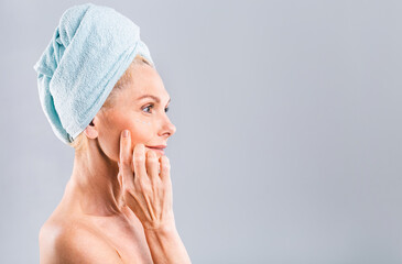 Portrait of smiling senior woman feeling soft skin with hand after spa bath. Mature woman draped in towel hair looking at camera. Lady in bathrobe after shower isolated over white background.