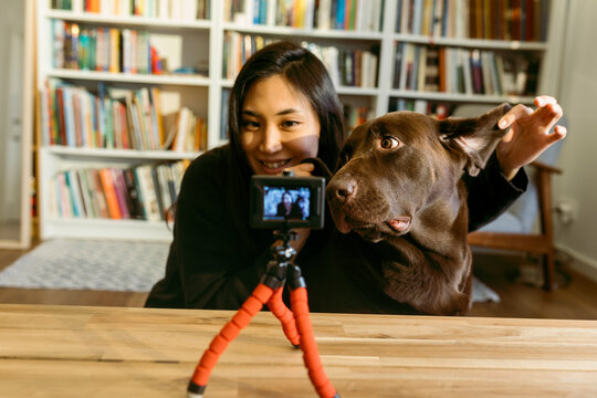 female east asian woman and her labrador dog at home recording a video