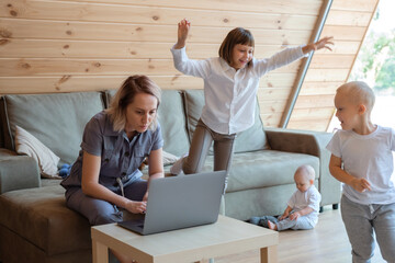 Serious woman using laptop near playing children at home