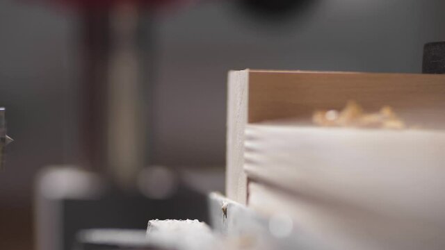 The drilling machine makes a hole in a wooden board. The drill moves on the side of the tree. Making a furniture. Bore the holes, mechanical processing of timber.