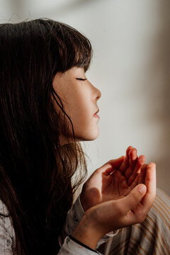 Portrait of a little girl with dark hair closed eyes and joined hands reflecting light to the face