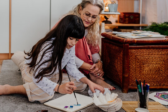 Little girl painting mandalas with her grandmother at home