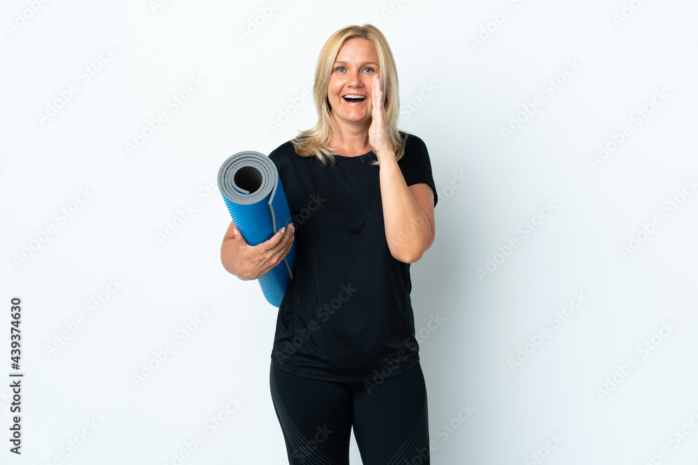 Wall mural Middle age woman going to yoga classes while holding a mat isolated on white background shouting with mouth wide open