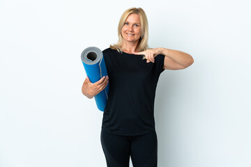 Middle age woman going to yoga classes while holding a mat isolated on white background and pointing it