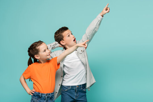 happy girl and amazed boy pointing with fingers while looking away isolated on blue.