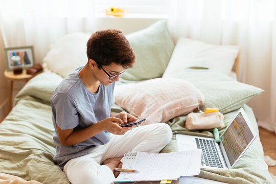 Teenager with studies on bed texting on phone
