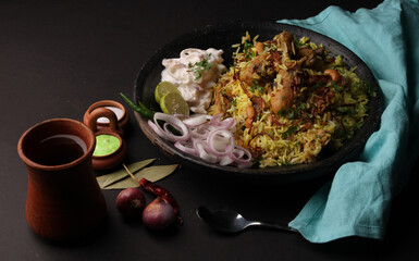 chicken dum biriyani served in copper handi or bowl with onion raita.