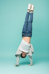 happy boy in denim jeans doing handstand on blue.