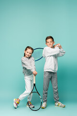 cheerful kids in sportswear standing with tennis rackets on blue.