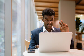 Portrait of African businessman using laptop computer in coffee shop while waving and having video call