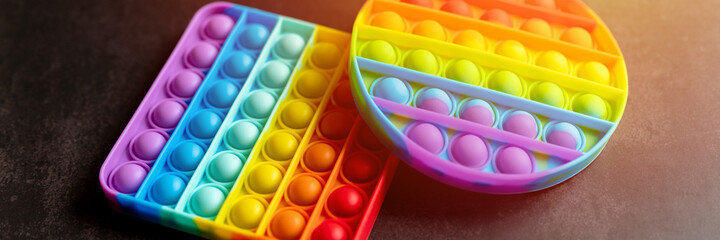 kids anti stress sensory pop it or simple dimple fidget push toys on a black table or floor background. popit rainbow hue bright color, trend 2021 year. top view, flat lay. banner. flare