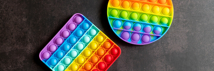 kids anti stress sensory pop it or simple dimple fidget push toys on a black table or floor background. popit rainbow hue bright color, trend 2021 year. top view, flat lay. banner