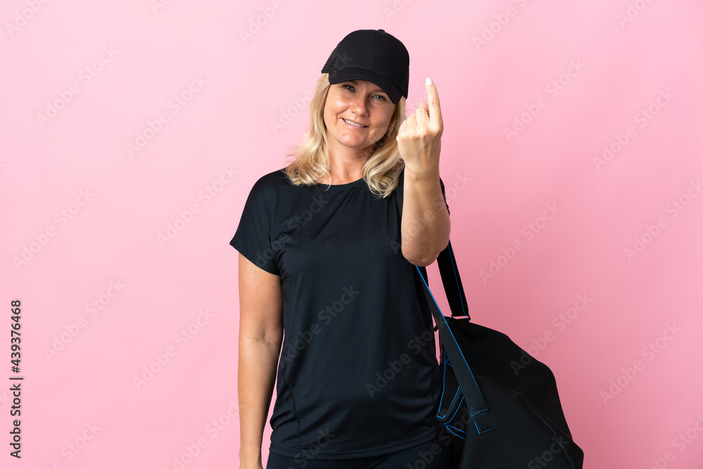 Wall mural Middle age woman with sport bag isolated on pink background doing coming gesture