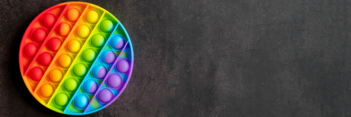 kids anti stress sensory pop it or simple dimple fidget push toy on a black table or floor background. round popit rainbow hue bright color, trend 2021 year. top view, flat lay. space for text. banner