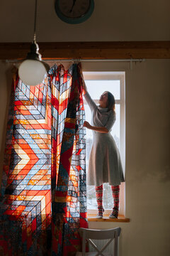 A woman hangs a curtains on the window.