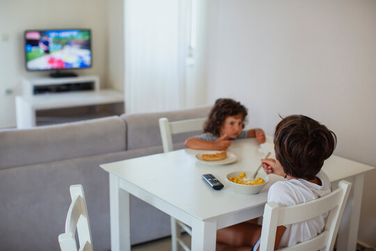 Nine year old boy watching tv while eating breakfast