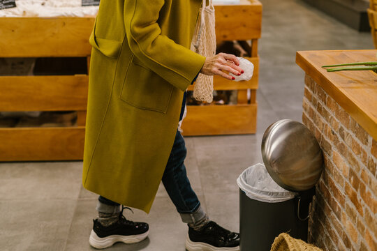 Close-up of senior woman throwing hygiene gloves in the bin at waste store