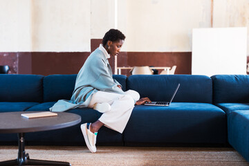 Stylish black freelancer on couch with laptop