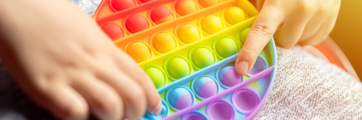 anti stress sensory toys in a children's hands. a little happy kid boy plays with a toy in the car. toddler holding and playing trendy rainbow color. banner. flare