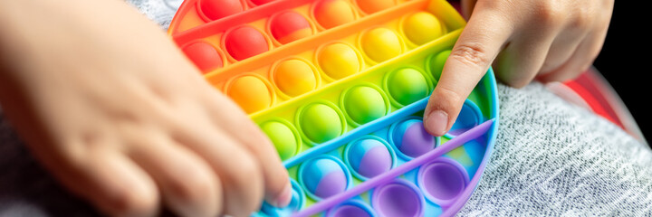 anti stress sensory pop it toys in a children's hands. a little happy kid boy plays with a simple dimple toy in the car. toddler holding and playing popit rainbow color, trend 2021 year. banner