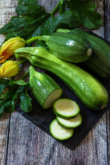 Harvesting zucchini. Healthy uncooked fresh green zucchini with slice on a wooden kitchen table. Copy space.