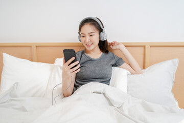 Young asian woman with headphones relaxing at home. listening to music in bed