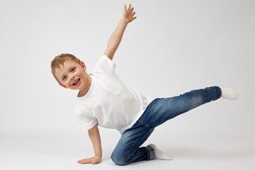 Happy child with blue eyes and a toothy smile is doing fitness on a white background. The boy in...