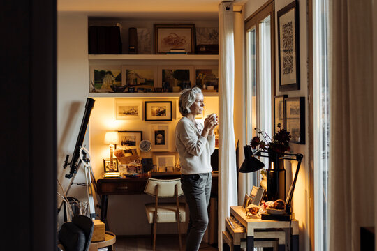 Mature woman with cup of drink near window