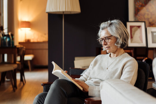 Peaceful middle aged woman reading book in cozy living room