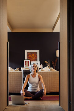 Mature fit woman relaxing in Lotus pose with closed eyes at home