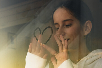 teenager girl looking trough window painting a heart 
