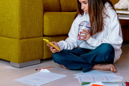 teenager girl drinking a smoothie and doing her homeworks at home 