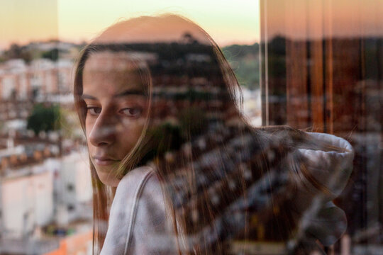 Teenager girl whit reflection of the city looking trough window 