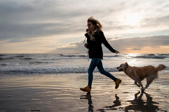 Woman runs on the beach with her dog