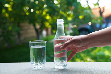 Hand holding drinking water bottle on green nature background.