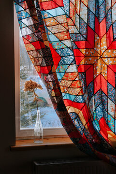 A window with a multicolored patchwork curtain.