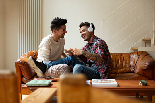 Happy couple of gays with smartphone chilling on couch
