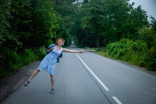 Beautiful blonde travel woman hitchhiking on the road.  Horizontal image.