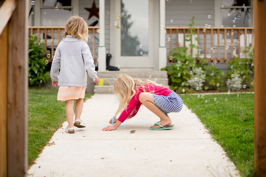 Girl draws with sidewalk chalk on front path