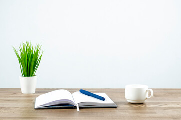 Open notebook and pen on the table. Flowerpot in a white pot. Desktop. Office.