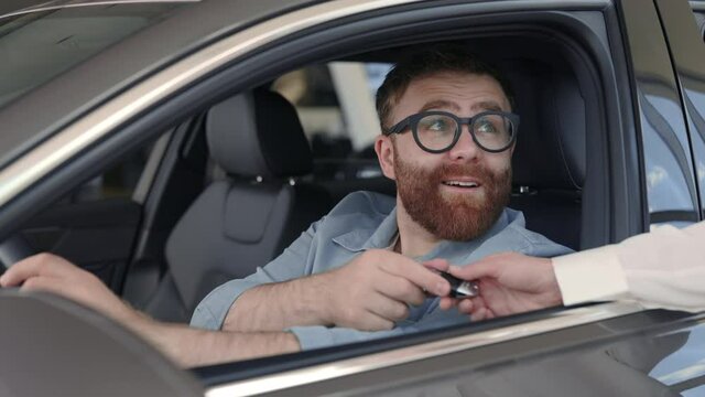 Man sitting in new car and taking keys from female seller