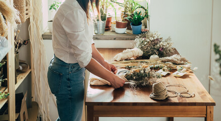 Unrecognizable Female Florist Wrapping Everlasting Bouquet of Dried Flowers at Wooden Table at her Flower Shop.
Side view of cropped woman entrepreneur arranging bouquet of a dry flowers and plants.