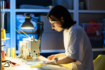 Needlework process in design studio: young female seamstress work on sewing machine, sew clothes....
