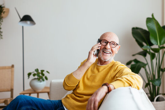 Happy aged male speaking on smartphone on couch